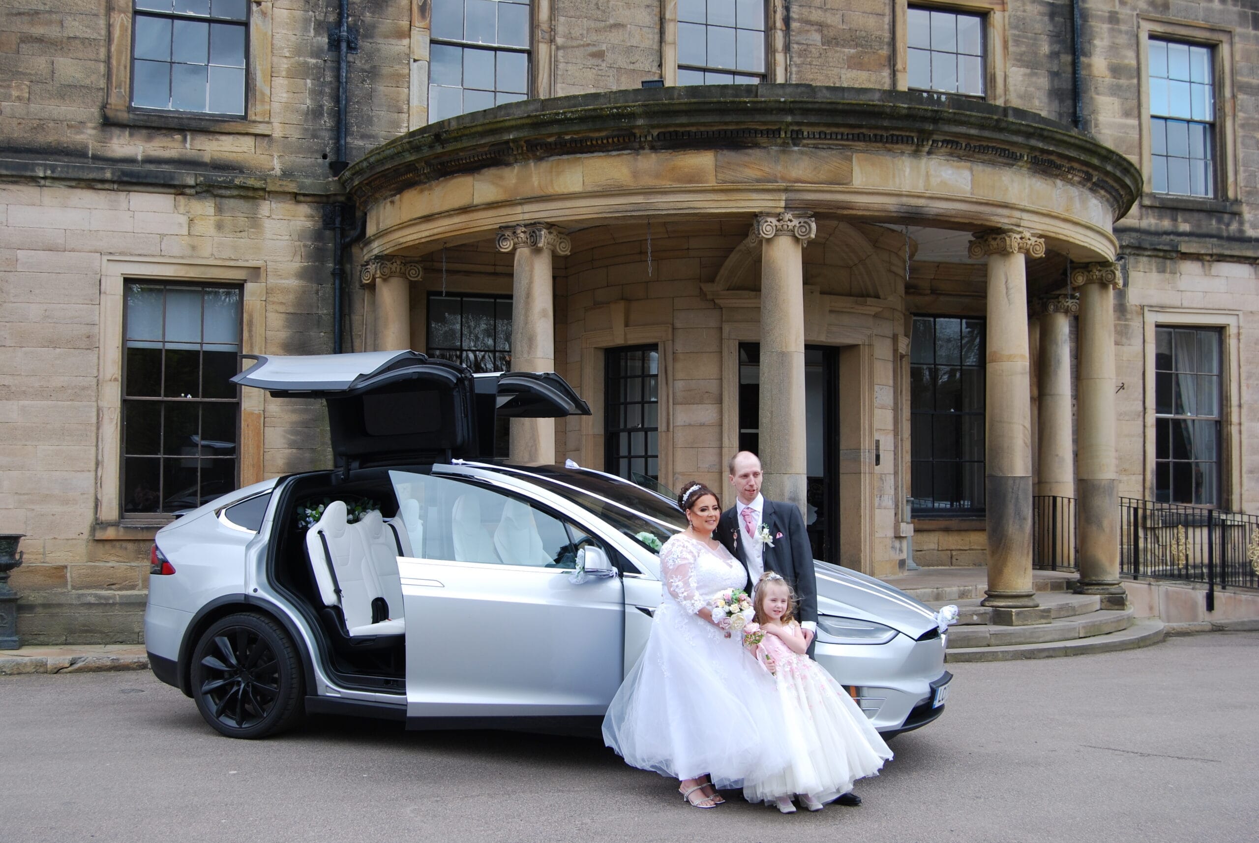 Bride and groom with Tesla wedding car at a weekday ceremony, smiling outside a quiet venue